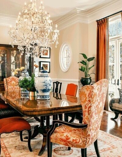 A formal dining room with orange chairs and a chandelier.