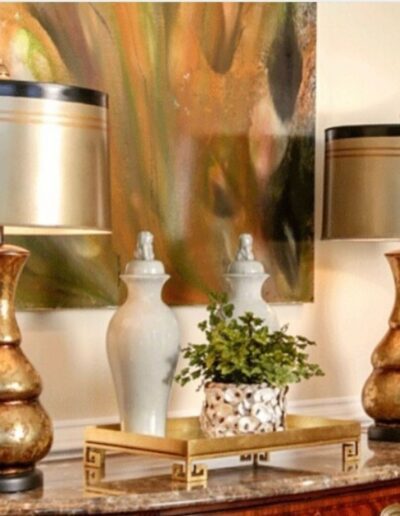 Two gold lamps on a table with a painting on the wall.