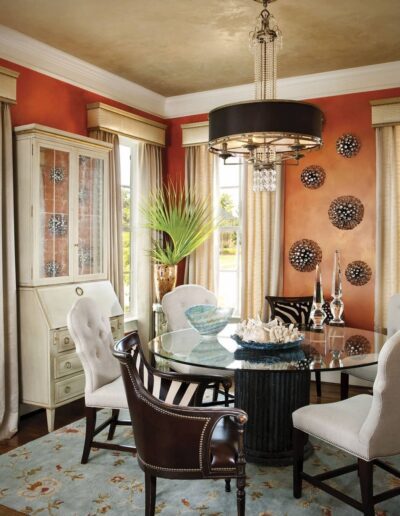 A dining room with orange walls and zebra print chairs.